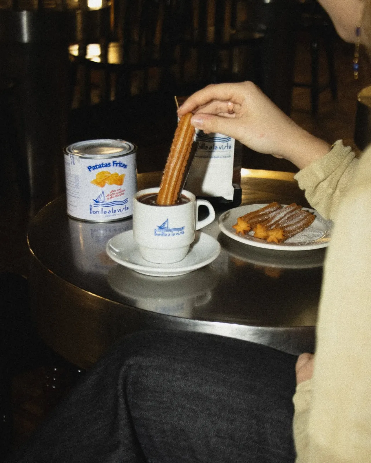Churro mojado en chocolate con lata de patatas Bonilla a la vista al lado