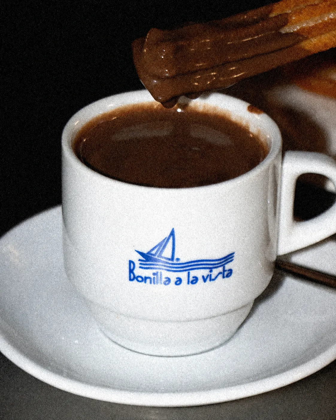 Taza Bonilla a la vista con chocolate caliente y un churro mojado